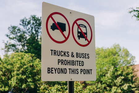 A sign bans trucks and buses beyond this point, set against a backdrop of lush green trees and a blue sky.の写真素材