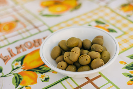 Green olives in a bowl on a bright lemon-patterned tablecloth, ideal for a summer gathering with friends.の写真素材