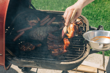 Meat is being grilled in a backyard, smoky aroma fills the air during a sunny afternoon gathering.