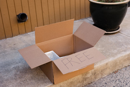 Cardboard box placed outside with a sign indicating free items available for anyone passing byの写真素材