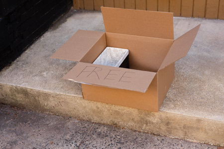 Cardboard box with a free sign on the sidewalk displaying an empty container in a neighborhood settingの写真素材