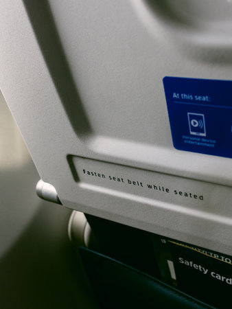 A close-up view of a seat belt reminder in an airplane, highlighting safety instructions for passengers while in flight.の写真素材