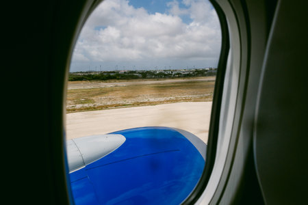 Blue airplane wing visible out the window as it approaches landing on a sunny day at an airport with...