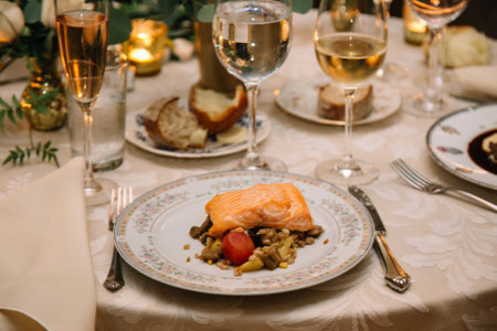 Delicious salmon served with vegetables and wine on a beautifully set dining table with candles and flowers.の写真素材