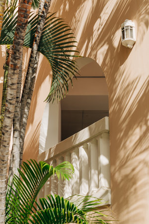 Palm leaves cast shadows on a textured peach wall where a balcony can be seen, creating a serene tropical atmosphere.の写真素材