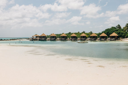 Tropical bungalows line the shore, inviting visitors to enjoy the calm waters and bright skies on a sunny day.の写真素材