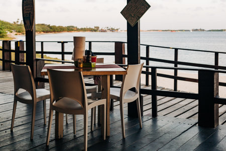 A cozy dining arrangement by the beach with chairs and a table overlooking the calm sea at dusk.の写真素材