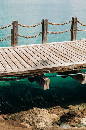 A sturdy wooden dock stretches over calm turquoise water, providing a peaceful escape by the rocky shoreline.の写真素材