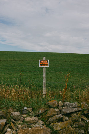 A rustic sign indicating private property stands against a backdrop of a vast green field under cloudy skies.の写真素材