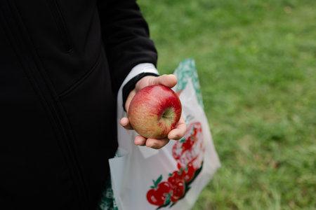 Individual enjoys a fresh red apple after selecting it from a local outdoor market in the crisp...