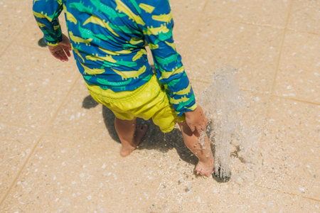 A young child in a colorful swimsuit joyfully plays in a water feature on a sunny day, enjoying the splashes.の写真素材