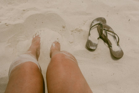 Feet nestled in soft white sand with flip-flops resting beside them on a calm beach in the afternoon...