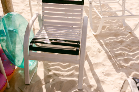 A beach chair sits on the soft sand with bright floaties positioned beside it, showcasing a perfect...