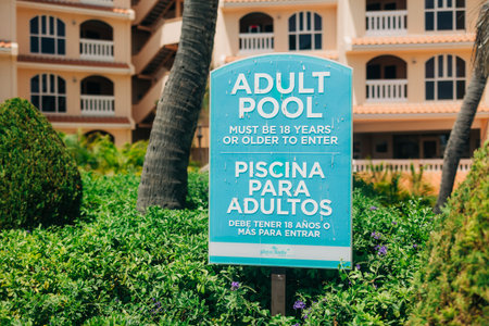 Sign instructs that only adults aged 18 or older may use the pool, surrounded by lush green plants.