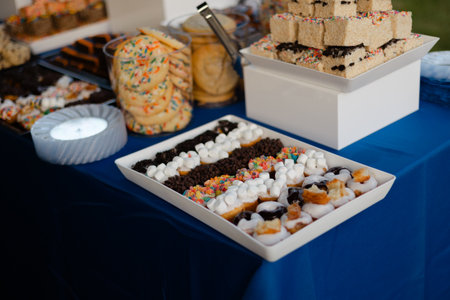Delicious cookies, cakes, and colorful toppings are on a blue table at a joyful event.の写真素材