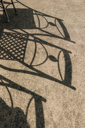 Chairs with intricate patterns create striking shadows on warm pavement in a sunlit outdoor area.