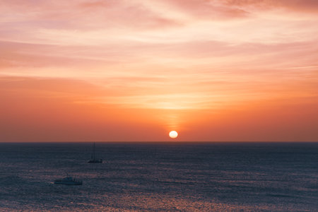 A breathtaking sunset displays vibrant colors over the ocean as sailboats drift gently in the water.の写真素材