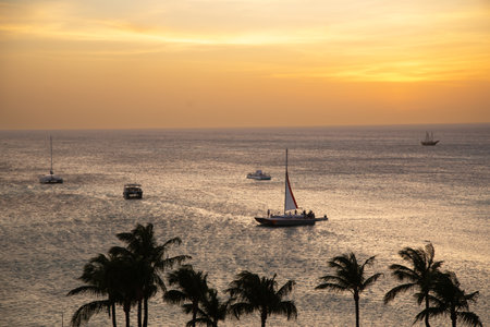 Sailboats glide across tranquil waters as the sun sets behind the horizon, creating a serene coastal...