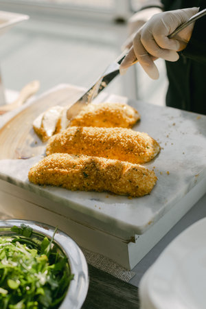 Freshly cooked crispy fish fillets are being sliced and served alongside a bowl of vibrant greens.