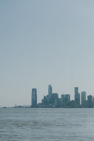 Skyline shows tall buildings by calm waters under a clear sky, capturing urban beauty and serenity.