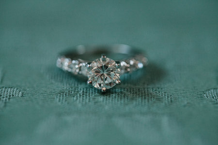 Elegant diamond engagement ring displayed on teal fabric background, highlighting its intricate...