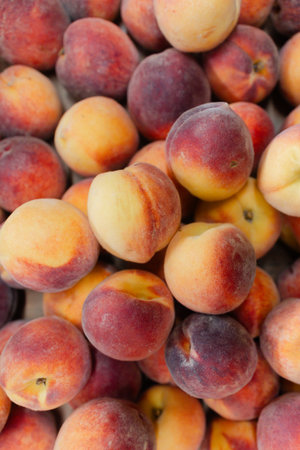 Vibrant peaches are displayed in a market, showcasing their rich colors and freshness under bright...