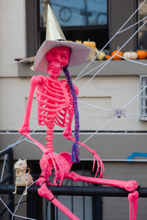 A vibrant pink skeleton wears a paper hat and is surrounded by autumn decorations on a balcony...