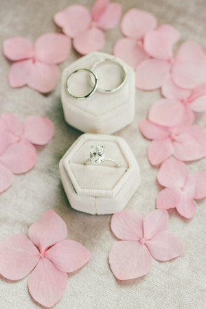An engagement ring with a sparkling center stone and wedding bands on soft pink petals.の写真素材