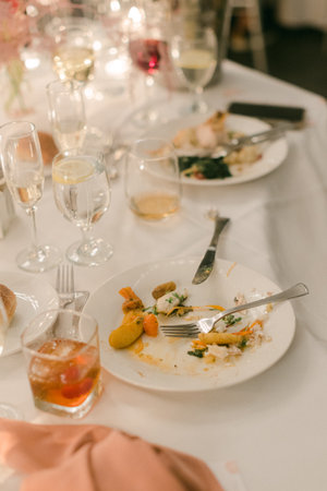 Plates with remnants of dinner are cluttered on the table amid glasses of beverages and candlelight.の写真素材