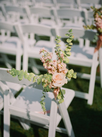 Floral arrangements adorn white chairs, enhancing the romantic atmosphere of an outdoor wedding ceremony.の写真素材