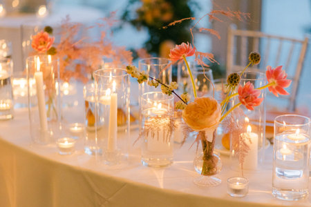 A beautifully arranged table featuring glowing candles and fresh flowers creates a warm atmosphere for guests.の写真素材