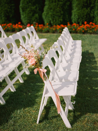 Colorful flowers adorn white chairs in neat rows, creating a charming atmosphere for a garden wedding celebration.の写真素材
