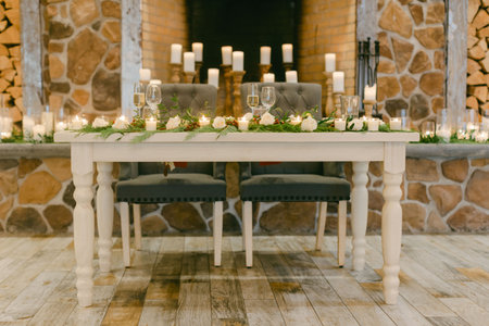 Beautifully arranged table for a wedding reception featuring candles, flowers, and a cozy fireplace backdrop.の写真素材