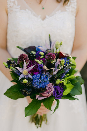 The bride carries a beautiful bouquet of purple and blue flowers, enhancing the wedding's elegance.の写真素材