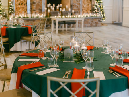 Elegant tables adorned with green and red decorations set for a holiday celebration at a beautiful venueの写真素材
