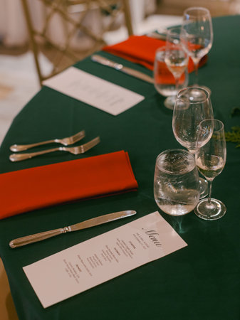 Beautifully arranged dining table set for a formal event with red napkins, glassware, and a menu displayed.の写真素材