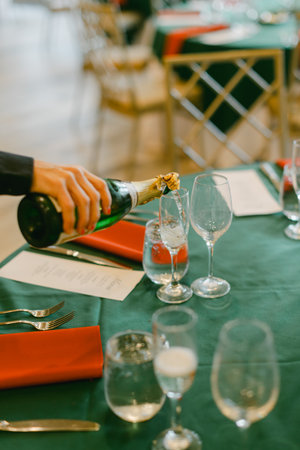 A hand pours champagne into glasses at a beautifully set table, creating a festive atmosphere for guests.の写真素材