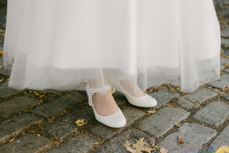 A bride's exquisite white shoes are partially visible under her sheer flowing dress on a charming cobblestone path.の写真素材