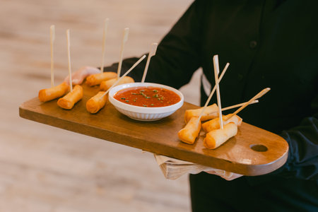 A server brings a wooden platter of spring rolls and a bowl of red dipping sauce, ideal for sharing.の写真素材