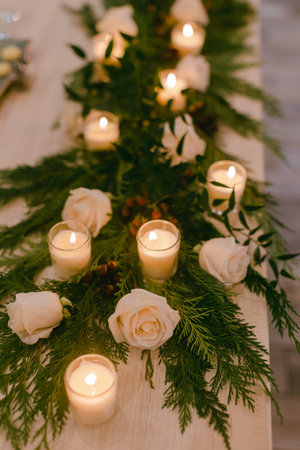 Beautiful arrangement of white roses and lit candles on a wooden table, creating a warm atmosphere for guests.の写真素材