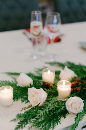 A beautifully arranged table features white roses, glowing candles, and lush greenery, perfect for a festive gathering.の写真素材
