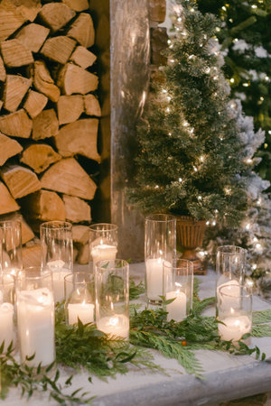 Candles and greenery create a warm atmosphere for a holiday celebration near stacked logs and a softly lit tree.の写真素材