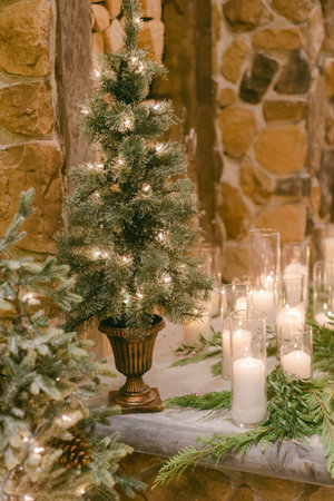 Cozy setup with small illuminated trees and candles placed on a table adorned with greenery in a rustic setting.の写真素材
