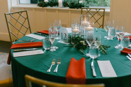 A beautifully arranged holiday table features red napkins, elegant glassware, and a centerpiece of greenery and candles.の写真素材