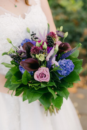 A bride holds a colorful bouquet of flowers, including roses and lilies, while enjoying a sunny outdoor moment.の写真素材