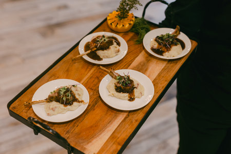 Waiter presents beautifully plated lamb chops on creamy mashed potatoes to eager diners in an inviting setting.の写真素材