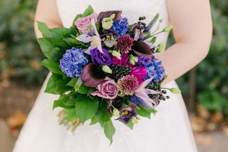 A woman in a wedding dress holds a vibrant bouquet of purple and blue flowers surrounded by greenery.の写真素材