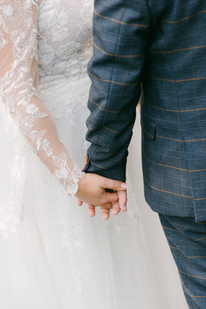 A couple in elegant wedding attire holds hands, surrounded by a romantic outdoor setting.の写真素材