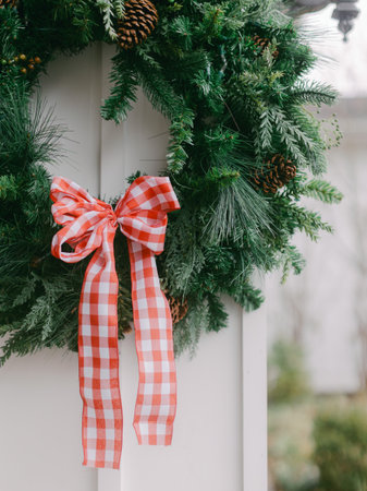 A vibrant wreath decorated with a red checkered bow is hung on a door, enhancing the festive atmosphere during winter.の写真素材