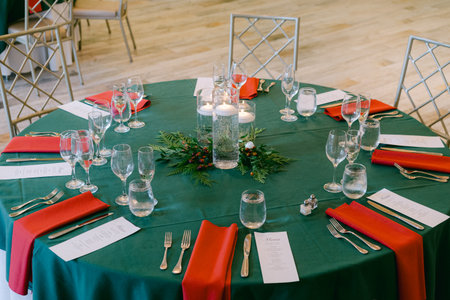 Round table elegantly arranged with red napkins, glasses, and candles, ready for holiday dining in a...
